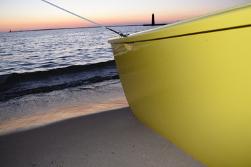 Boat on shore with a lighthouse in the background at sunset.