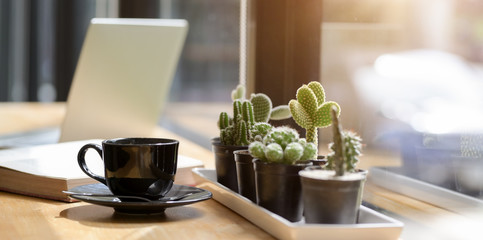 Coffee cup with cactus in black pot in comfortable workplace with tablet in the background