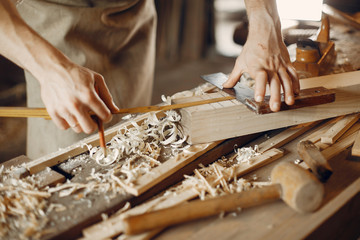 Man working with a wood. Carpenter in a white shirt - obrazy, fototapety, plakaty