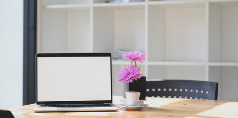 Open blank screen laptop computer in comfortable workspace with pink flower