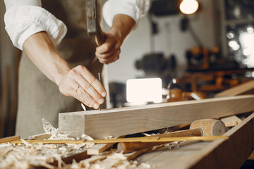 Man working with a wood. Carpenter in a white shirt. Man hammering nails into the wood