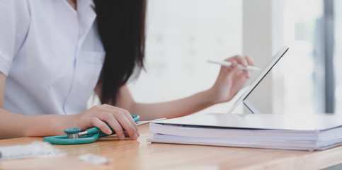 Close-up view of young female doctor examining the patient chart while using tablet