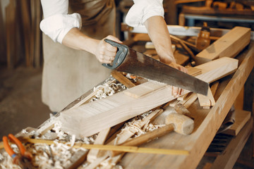 Man working with a wood. Carpenter in a white shirt. Worker with a saw