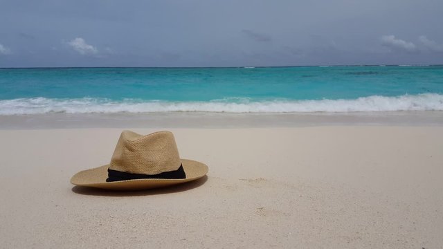 Design concept wallpaper with woven straw hat on white beach,turquoise ocean and blue sky background in Haiti