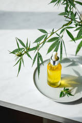 Glass bottle with cannabis oil with hemp leaves on a marble background. Copy space.