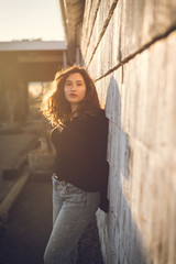 Young pretty woman portrait leaning against old building, backlit