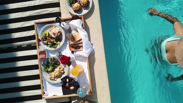 Attractive Woman in Bikini Approaching Poolside With Served Plentiful Breakfast Plate, Slow Motion Top Down Aerial View