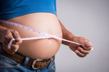 Overweight or fat adult man in very tight jeans with measuring tape on a gray background....