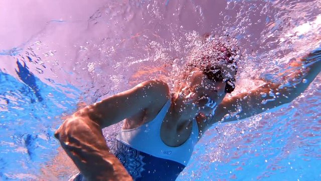 underwater bottom view of sport woman swimming crawl style in clear water of pool 