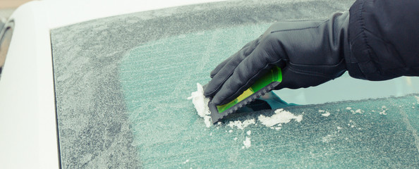 Hand of man using scraper to remove ice from window in car, winter problems