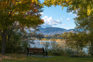 Empty park bench overlooking the beautiful view of the river, lake, bridge and mountains, green...