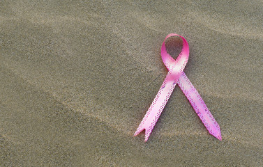 Breast cancer awareness month concept, pink ribbon on sand beach background, copy space text area.