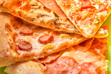 Four slices of different pizza. Pizza with mushrooms, pepperoni, ham, tomatoes. Slices of pizza are on a green plate.