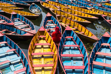 Fototapeta na wymiar colorful boats in Fewa lake in Pokhara, Nepal with women in red sitting inside