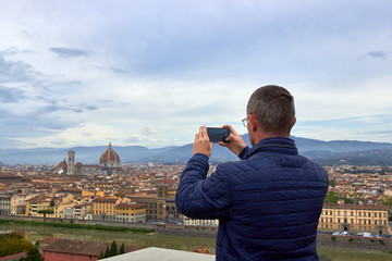 Man tourist taking a photo with a telephone of historical center of Florence in Italy from Piazzale Michelangelo. Back view.