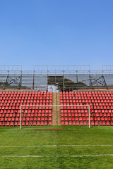 Soccer football goals in an empty stadium with red seats during the day with clear blue skies
