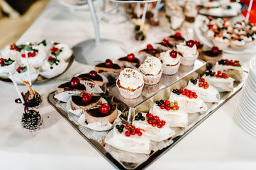 Sweet table. A plate of cakes and muffins with cream with berries. Table with sweets, candy, buffet. Dessert table for a party goodies for the wedding. Close up.