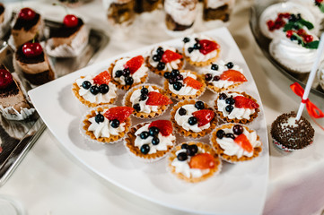 Sweet table. A plate of cakes and muffins with cream with berries. Table with sweets, candy, buffet. Dessert table for a party goodies for the wedding. Close up.