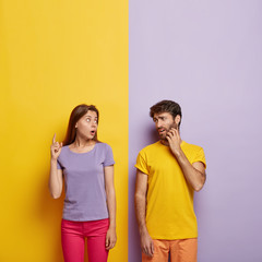 Photo of emotional impressed woman tries to explain something to man, points above with shocked...
