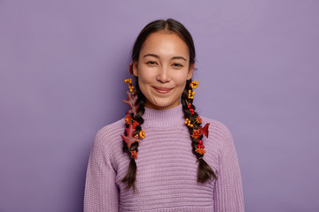 Glad natural Asian woman celebrates fall, finds inspiration in nature, has two plaits decorated...