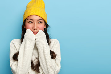 Indoor shot of lovely brunette woman wears yellow hat and white sweater, ready for winter stroll...