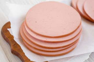 Pork bolgna meat slices on a rustic wooden board on a white wooden table, side view. Closeup.