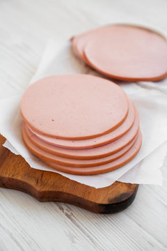 Sliced pork bolgna meat on a rustic wooden board on a white wooden background, side view. Close-up.