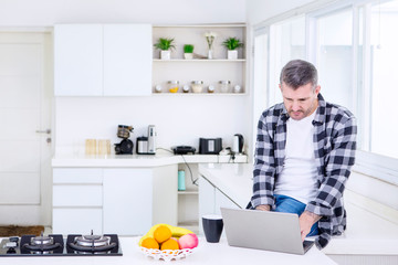 Caucasian man using a laptop in the kitchen
