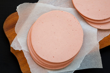 Sliced pork bolgna meat on a rustic wooden board on a black surface, top view. Flat lay, overhead, from above. © Liudmyla
