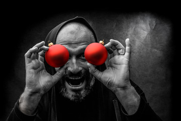 Black and white portrait of a bald bearded man in a hood with red christmas balls on a dirty gray background. Young Santa concept.