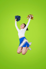 Cheerleader girl jumping with pom poms on studio