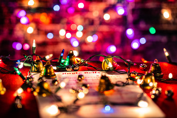 Jingle Bells Sheet Music lit by Christmas lights, surrounded by various bells.  Shallow depth of...