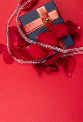 Wedding aniversary gift concept. Crystal necklace around blue gift box with rose petals on red background in top view