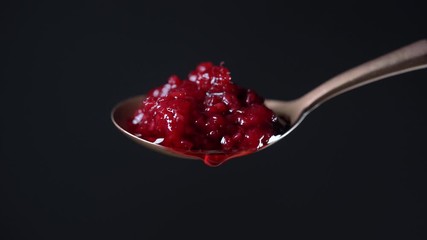 Spoon with red raspberry jam and one drop. Red raspberry jam dripping and flowing down from the metal spoon on black background, close up. Brass spoon with homemade red raspberry jam - Powered by Adobe