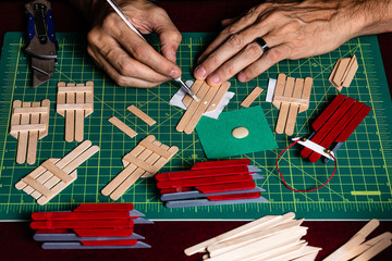 A tightly framed shot of someone working on crafts for the Christmas season.  Only the craftsman’s hands are visible in the shot while he glues and cuts craft sticks for building Snow Sled Ornaments
