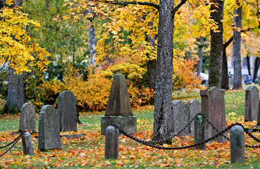 An old headstones in an old cemetery. Yellow autumn leaves on the ground.