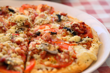 Pizza with mushrooms, tomatoes, spices on a white plate and a checkered tablecloth.