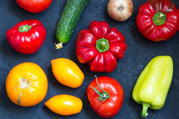 Fresh whole vegetables from new harvest on dark blue background. Washed pepper, tomatoes, onion and cucumber on table. Top view. Close-up. Raw foods, healthy meal concept. Vegan diet