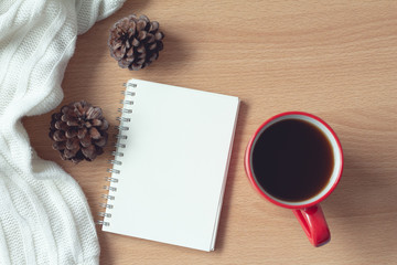 notebook with coffee,pine cone and white sweater on wood table background,office desk. Autumn and winter concept.