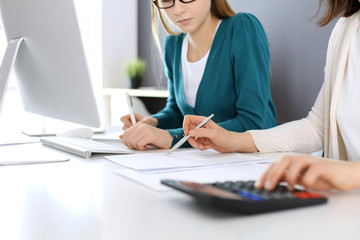 Accountant checking financial statement or counting by calculator income for tax form, hands close-up. Business woman sitting and working with colleague at the desk in office. Audit concept