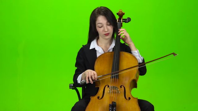Girl sits and plays the cello. Green screen