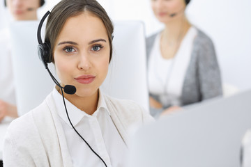 Call center. Group of operators at work. Focus on beautiful woman receptionist in headset at customer service white colored office. Business concept