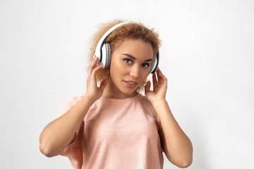 Freestyle. Young woman in headphones standing isolated on grey listening music looking camera curious close-up