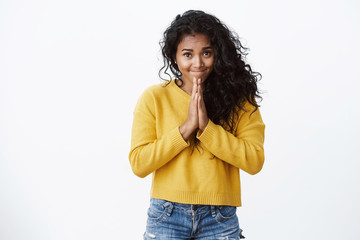 Pretty cute african-american curly-haired woman in yellow sweater press hands together in pray...
