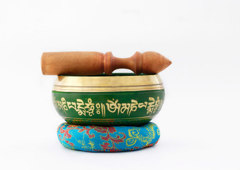 Hand made yellow and green Singing Bowl with written Tibetan language means mantra"om mani padme om" , used for meditation and yoga, with stick and multi color cushion as a base with  isolated white 