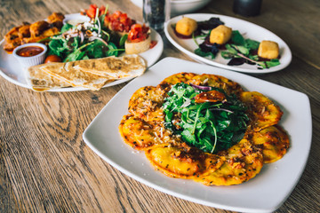 Porcini mushroom ravioli dish on wooden table with deep-fried brie and chicken wings plater in the background.