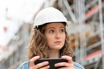 Pensive, thoughtful young civil engineer at work holding her mobile phone on construction site