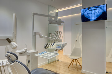 Fully equipped modern dental clinic box, with white walls and wooden floor. Dental radiograph shown on monitor.