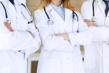 Group of modern doctors standing as a team with arms crossed in hospital office, close-up. Physicians ready to examine and help patients. Medical help, insurance in health care, best treatment and