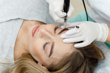 Permanent makeup, tattooing of eyebrows. Cosmetologist applying make up
